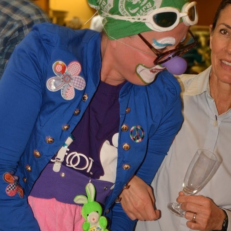 Clown mit grüner Mütze und gestreiftem Shirt, lächelt und hält Löffel.