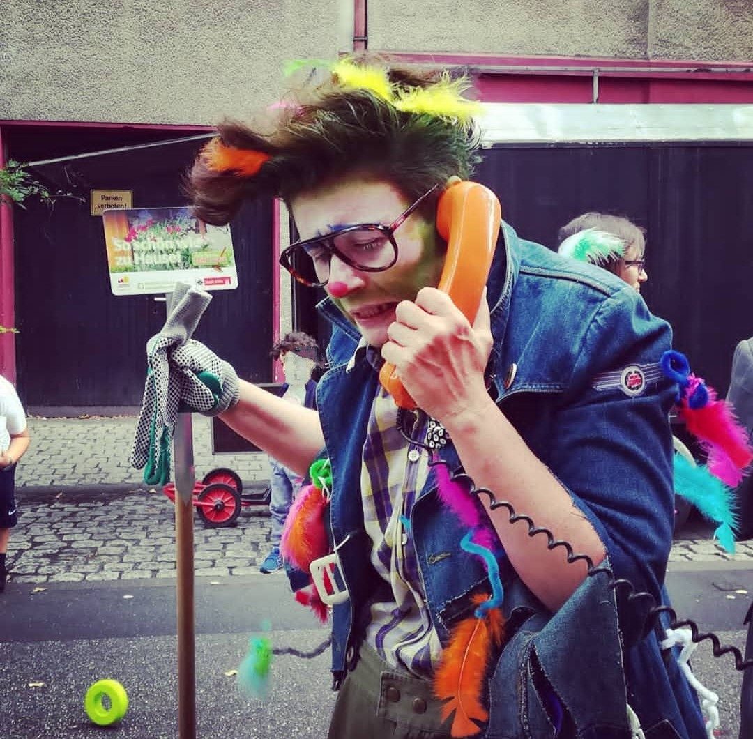 Person mit bunten Haaren trägt eine verrückte Maske und hält ein Telefon in der Hand.