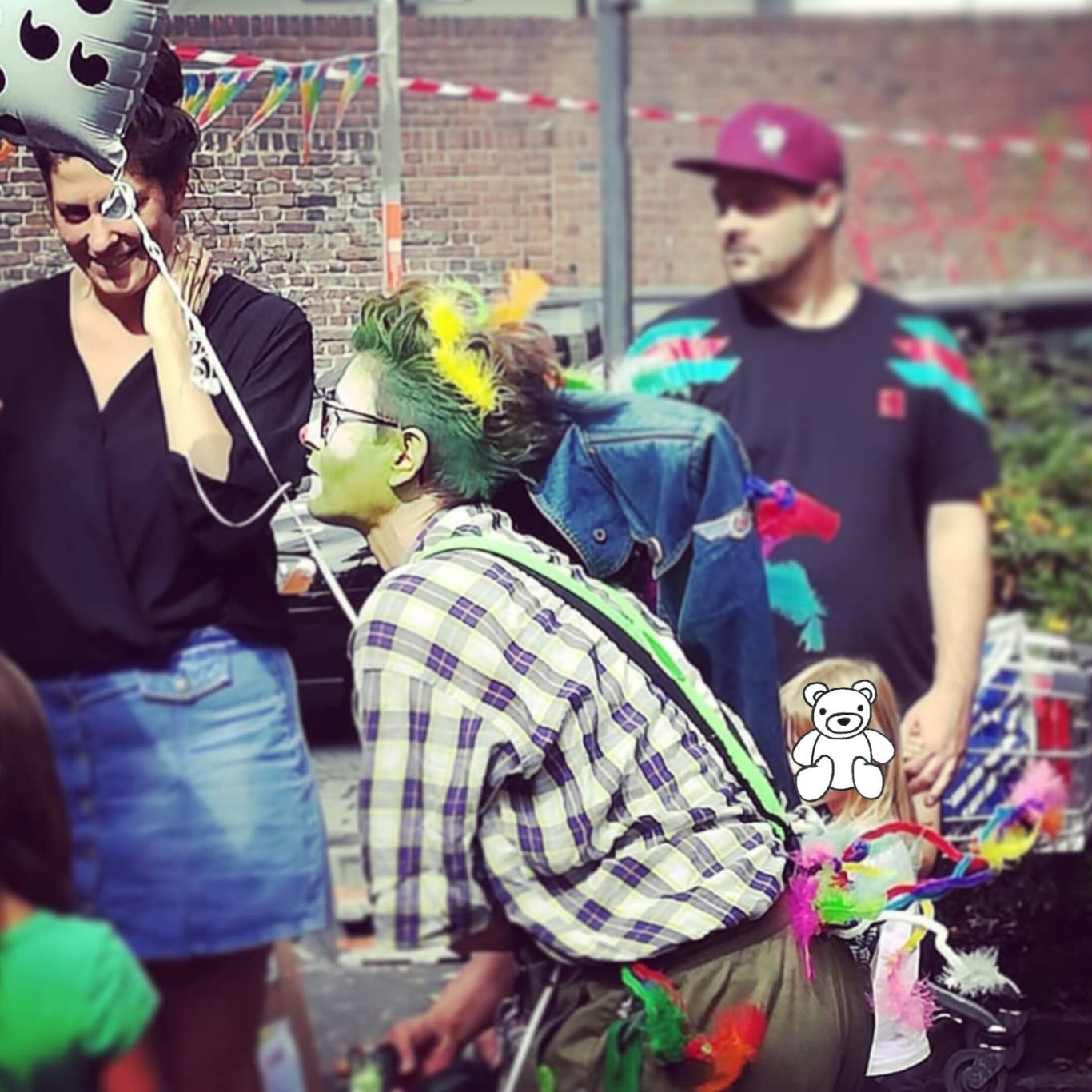 Eine Person mit bunten Haaren und Kleidern feiert mit anderen auf einem Fest.